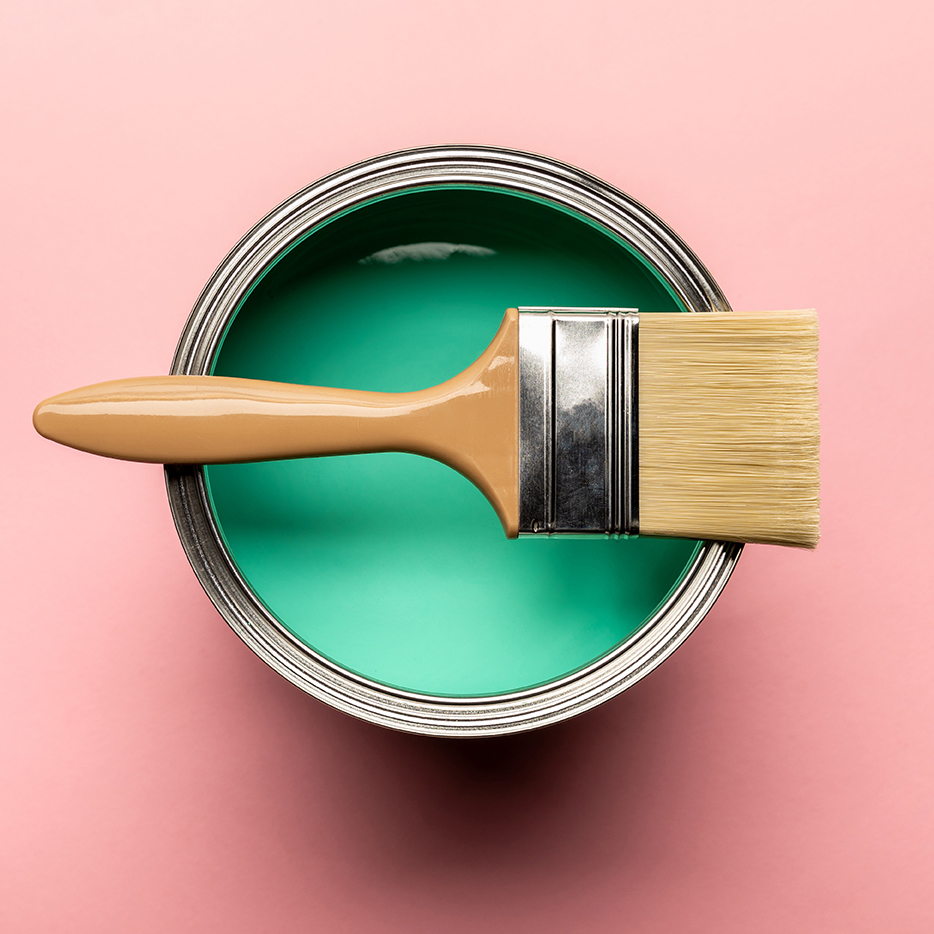top view of tin of green paint and brush on pink surface